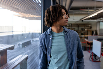 In office, African American man in casual attire looking out window thoughtfully