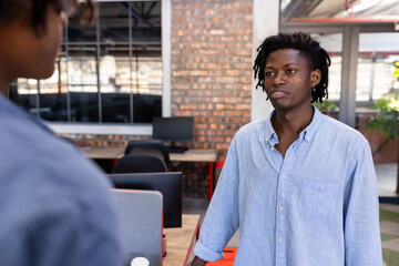 Discussing project, African American man in casual shirt with colleague in modern office
