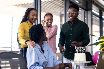 Colleagues celebrating birthday in office with cake, smiling and enjoying together