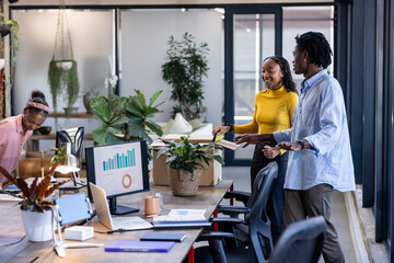 Collaborating colleagues discussing project with charts on computer in modern office