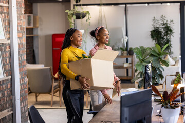 African American women carrying box with plant, smiling while moving into new office