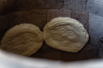 Fototapeta premium Uzbek flatbreads are baked in tandoor. They hang on wall of tandoor and begin to brown.