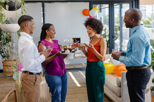 Colleagues celebrating birthday with cake and drinks in modern office lounge