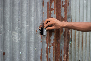 Hand reaching into a hole in a rusty corrugated metal wall