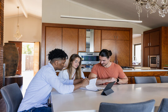 Diverse friends discussing project at home, using tablet and notebook on table