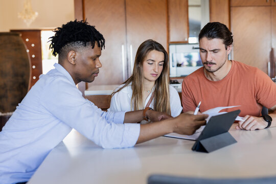 Diverse friends collaborating on project with tablet and documents at home - Powered by Adobe