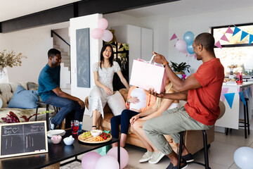 Friends celebrating baby shower at home, giving gifts and enjoying snacks together