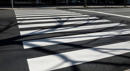 A pedestrian crosswalk with white stripes on asphalt, casting shadows from nearby trees.