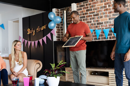 Friends playing baby shower game with chalkboard, enjoying festive indoor gathering - Powered by Adobe