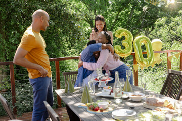 African American family celebrating birthday outdoors hugging with balloons and cake