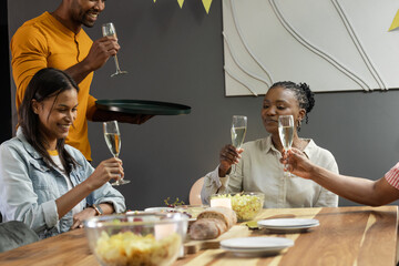 Friends toasting with champagne at dinner party, celebrating together joyfully