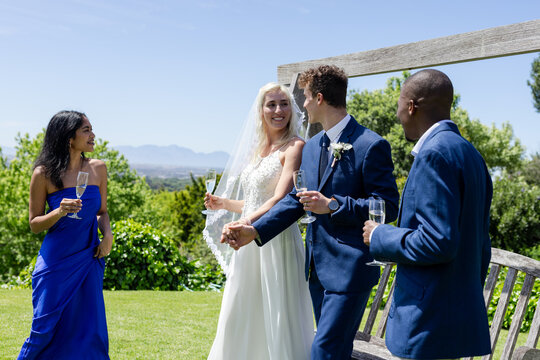 Bride and groom holding hands, celebrating with friends outdoors, enjoying champagne