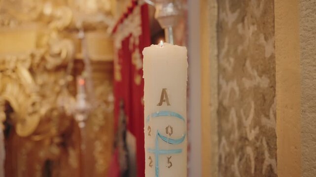 burning paschal candle marked with alpha omega and year inside ornate church