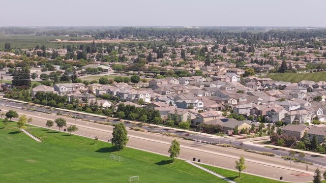 Drone receding from road toward soccer fields with residential view.