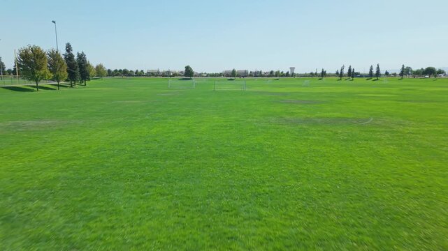 Low drone shot moving forward across soccer goals on green ground.