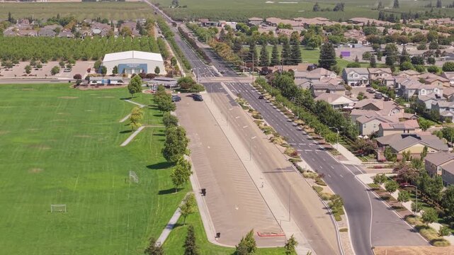 Aerial diagonal shot moving from soccer field to parking lot, road, and suburban houses in Ripon California.