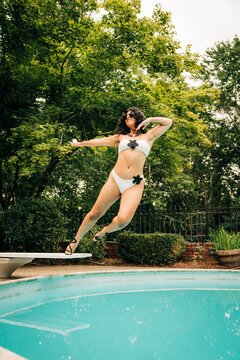 Young woman jumping into swimming pool on summer day