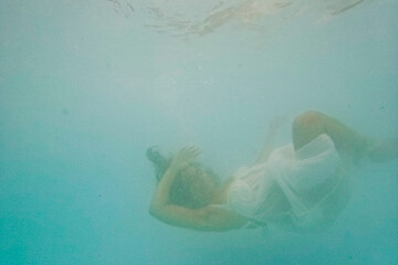 Woman wearing white dress floating underwater in swimming pool