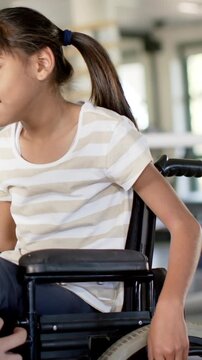 Turning child girl operating wheelchair at rehab gym, with parallel bars and equipment, copy space
