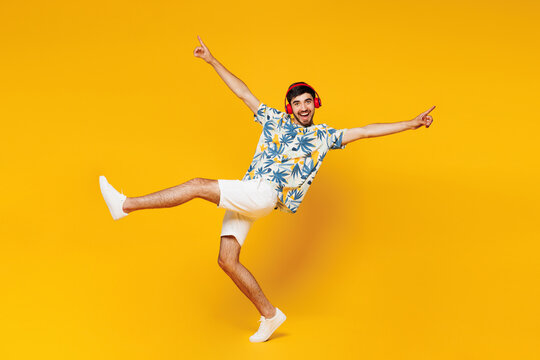 Full body young cheerful man wear blue beach t-shirt casual clothes listen to music in headphones raise up hands leg dance isolated on plain yellow orange background studio portrait Lifestyle concept