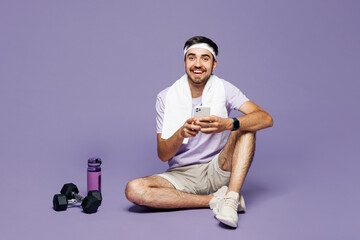 Full body young strong fitness trainer instructor sporty man sportsman wear sportswear train in gym sit hold use mobile cell phone isolated on plain purple background. Workout sport fit abs concept.
