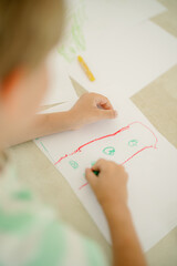 A young child focuses on drawing with crayons on a sheet of white paper. The artwork features bright colors and simple shapes, showcasing creativity in a calm environment.