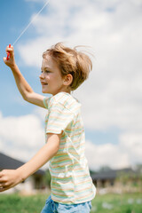 A young boy runs joyfully in a green field, holding a kite string. The sun shines brightly as fluffy clouds dot the sky, creating a cheerful atmosphere. It's a perfect day for outdoor fun.