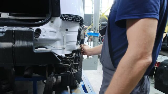 Mechanic touches rear of partially disassembled car with hand. Mechanic performs repairs to car and assess condition of body standing near vehicle