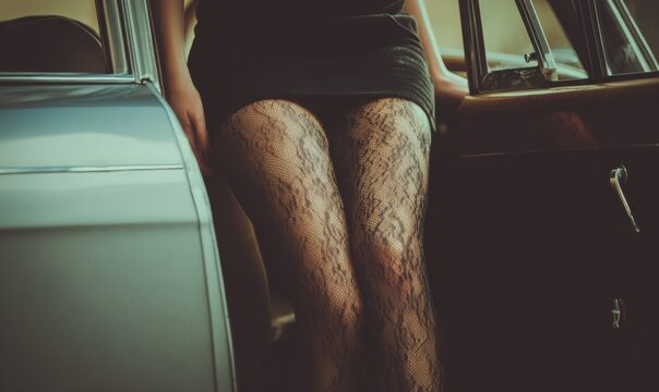 Fototapeta Woman in lace stockings posing by vintage car at sunset