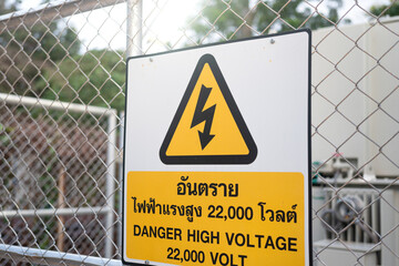 "Danger high voltage" warning sign which is installed on fence border of the electricity power control room at the industrial plant. Sign and symbol for industrial workplace, close-up.