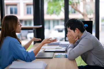 Stressed businessman covering face while businesswoman arguing in office meeting
