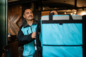 Deliveryman picking up food order in restaurant wearing thermal backpack