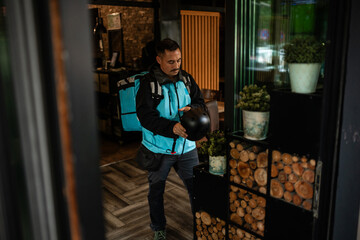 Deliveryman holding helmet entering restaurant after delivery
