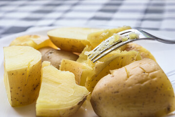 Delicious potatoes boiled in skins on kitchen table, closeup photo. Close-up fork with piece of soft boiled potato, homemade meal