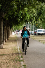 Delivery man riding bicycle in city park delivering food