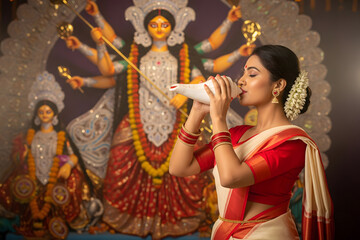 Obraz na płótnie Canvas Bengali Woman in Red and White Saree Playing Shankh During Durga Puja