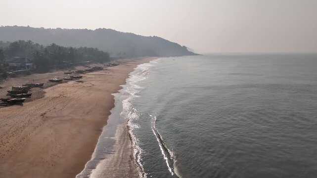 Serene aerial view of a deserted tropical beach at dawn, with gentle waves washing ashore along a forested coastline at Kelus Kalvi, India.