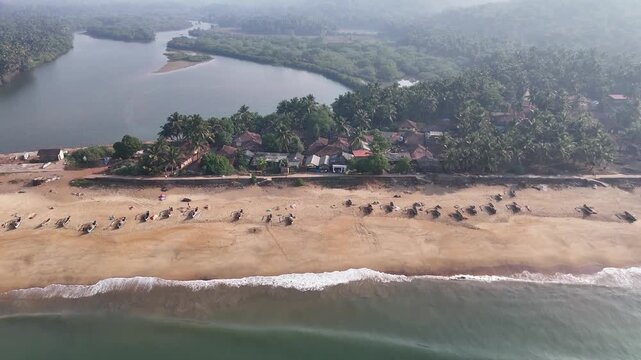 High-angle aerial view of a traditional fishing village on a sandbar between the ocean and a river at Kelus Kalvi Beach, India.