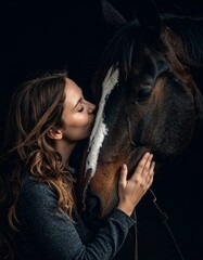 woman kissing nose of bay horse, portrait with black background