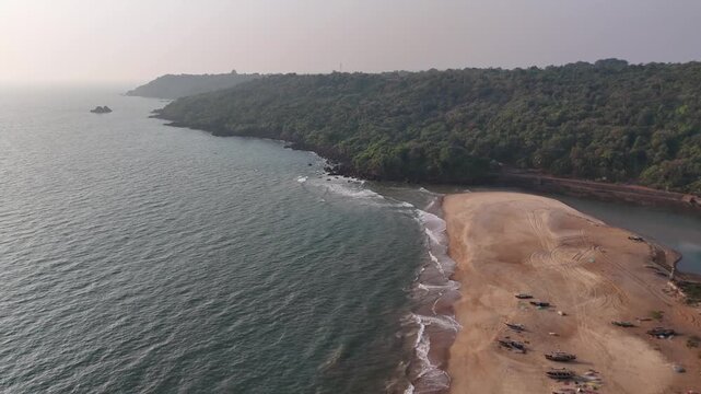High-angle aerial view of a traditional fishing village on a sandbar between the ocean and a river at Kelus Kalvi Beach, India.