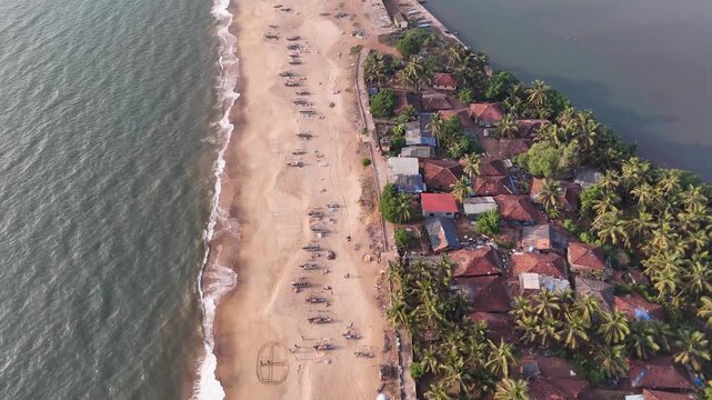 High-angle aerial view of a traditional fishing village on a sandbar between the ocean and a river at Kelus Kalvi Beach, India.