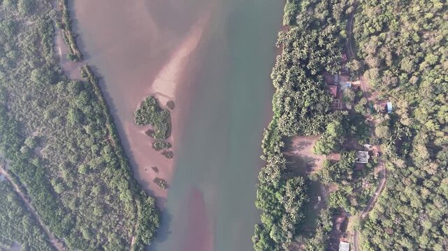 Top-down drone footage flying over a river estuary and a traditional fishing village, approaching the sandy shore of Kelus Kalvi Beach in India.