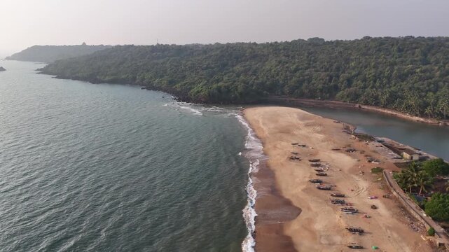 High-angle aerial view of a traditional fishing village on a sandbar between the ocean and a river at Kelus Kalvi Beach, India.