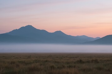 Fototapeta premium Fog covering a meadow at sunrise with mountains in the background