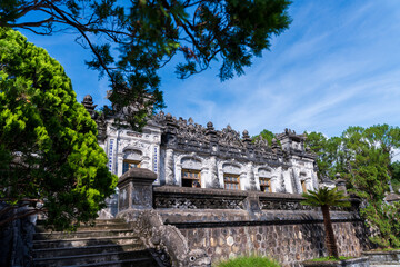 Fototapeta premium A broad view of the Khai Dinh Tomb's intricate, ornate exterior, with its detailed stone carvings and grand staircase under a striking blue sky.