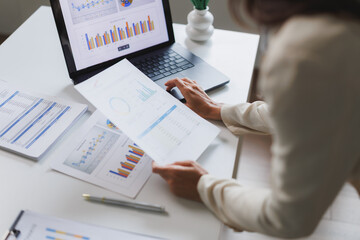 Businesswoman analyzing financial charts and data on laptop and documents