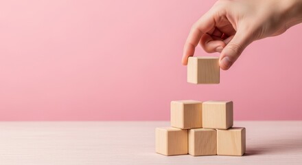 Hand placing a wooden block on a stack against a pink colored background