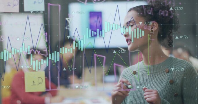 Sketching charts, woman wearing green sweater writing on glass panel in office, with sticky notes