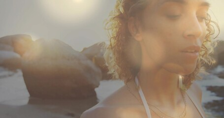 Standing woman gazing at ocean near beach cove, wearing swim top with layered necklaces, copy space