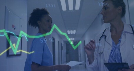 Reviewing nurse and doctor in medical attire analyzing line graph in hospital corridor, with tablet